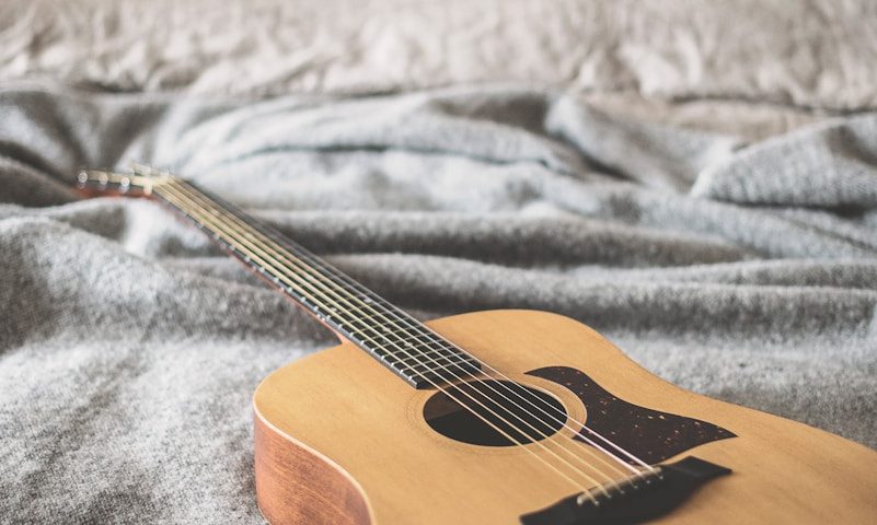 brown acoustic guitar on gray blanket