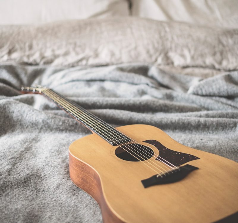 brown acoustic guitar on gray blanket
