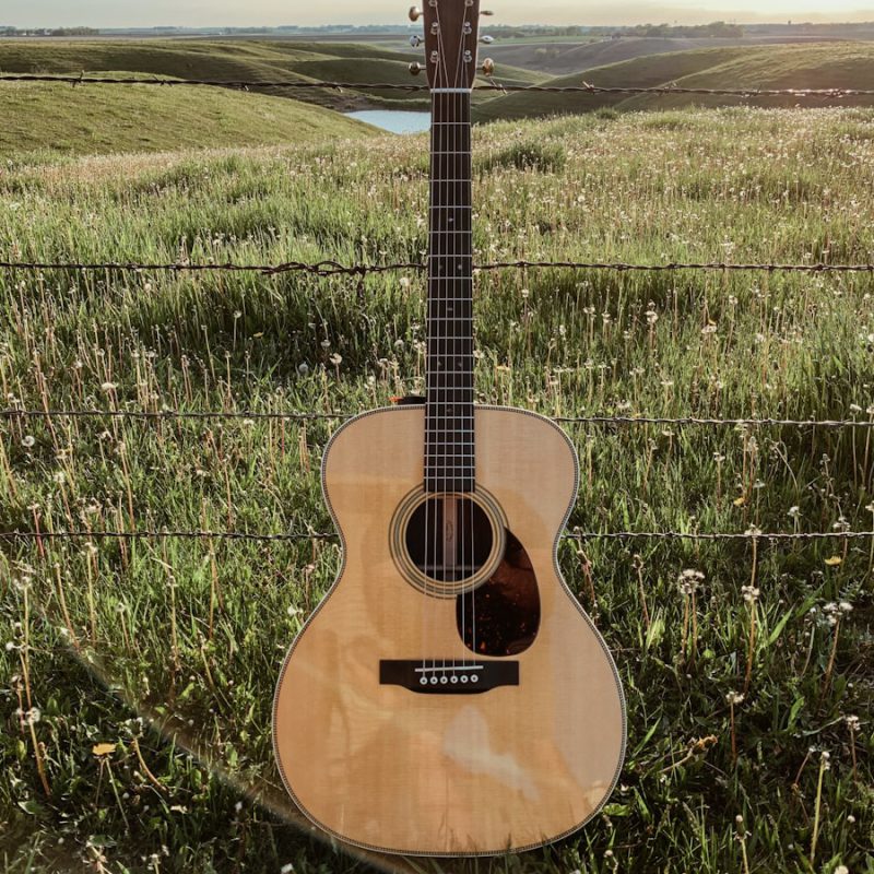 brown acoustic guitar on green grass field during daytime